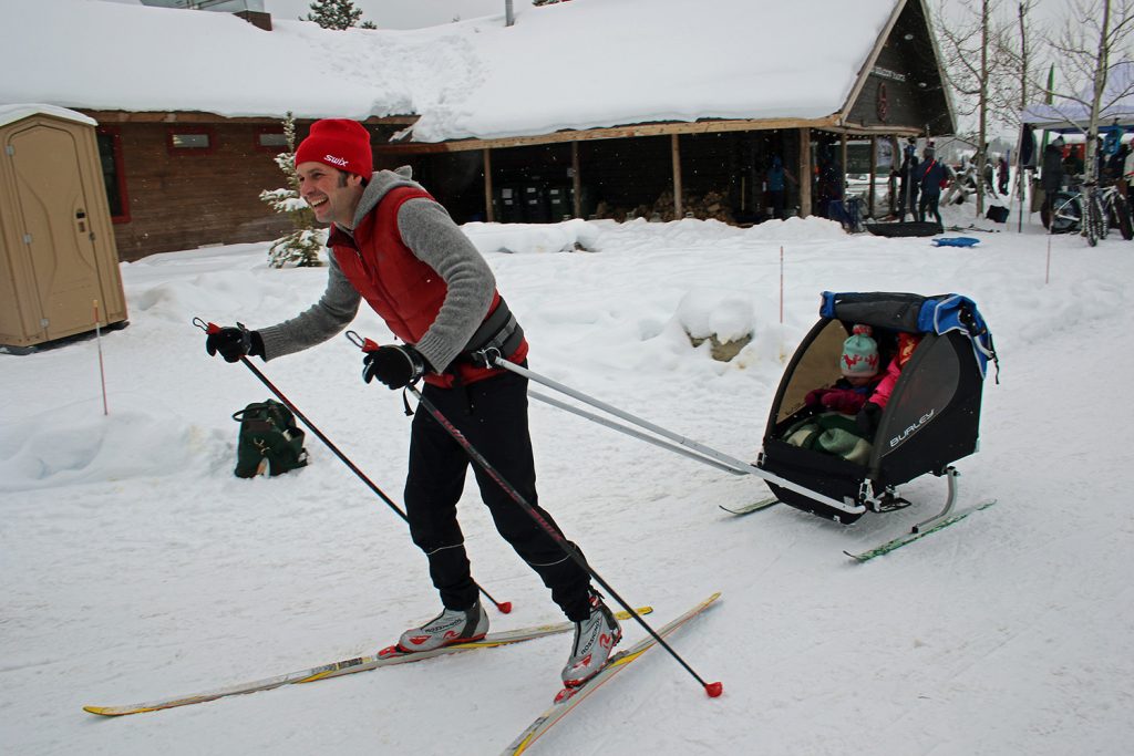 A father skiing and pulling children in a chariot on skis behind him