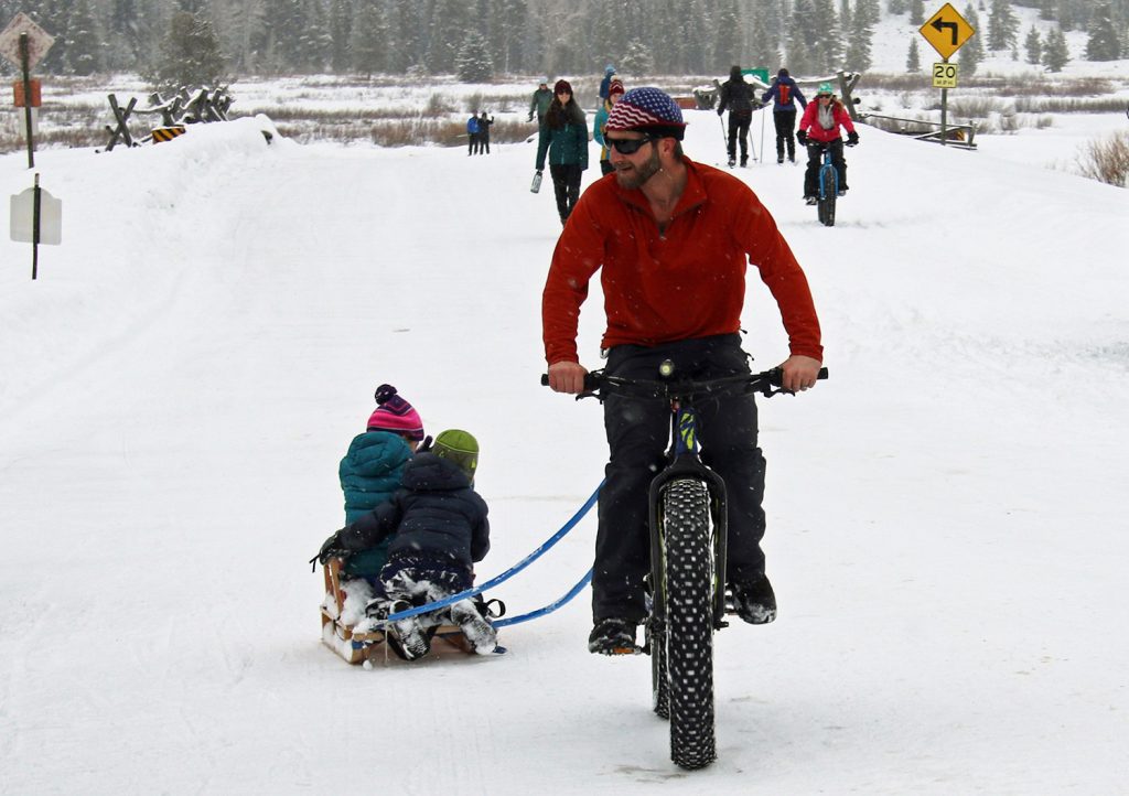 At the JH Nordic Free Ski, Fat Bike, Snowshoe Day, a father on a fatbike pulling children behind on a sled